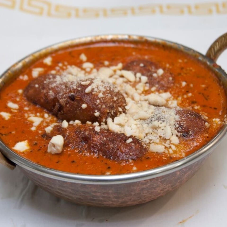 Indian malai kofta in a copper bowl, topped with crumbled cheese and a rich orange sauce.