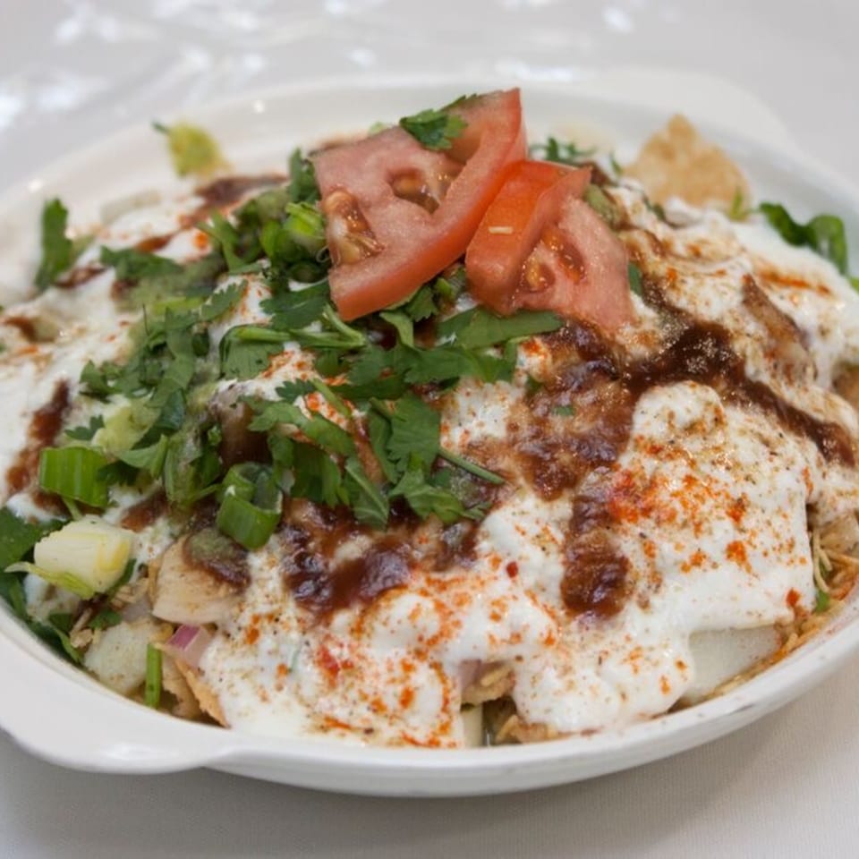 Bombay Chaat House's Indian chaat dish, topped with yogurt, chutney, tomatoes, and fresh herbs.
