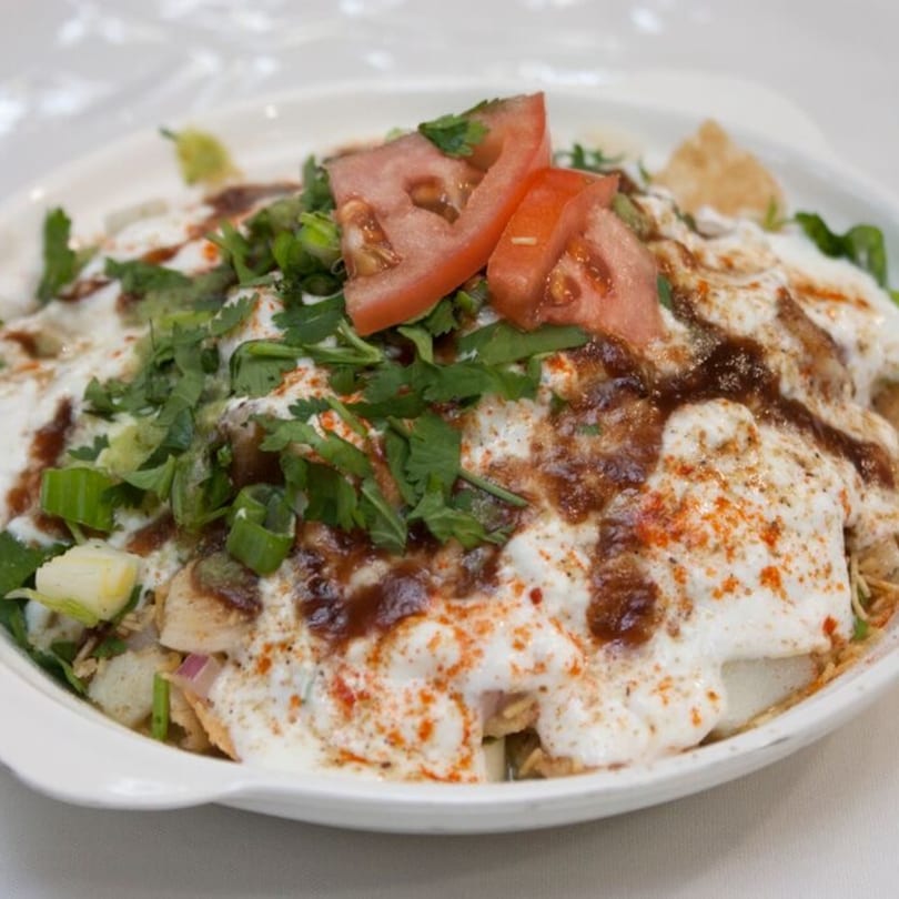 Bombay Chaat House's Indian chaat dish, topped with yogurt, chutney, tomatoes, and fresh herbs.