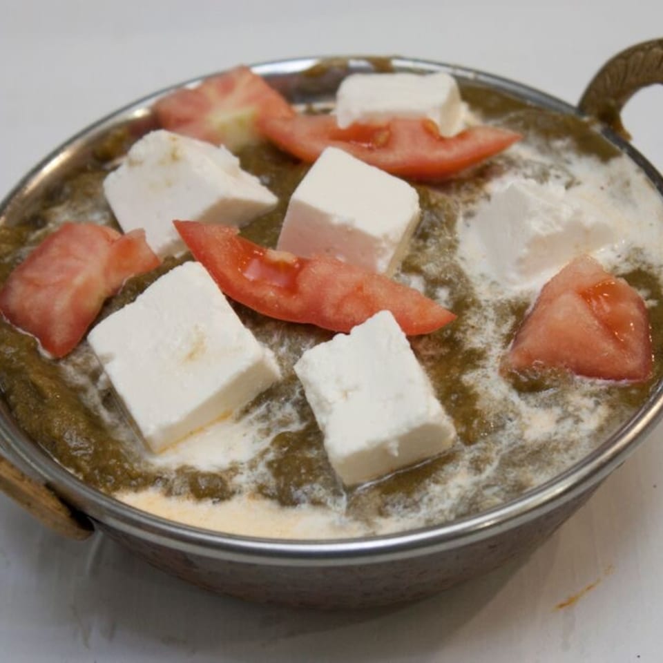 Palak Paneer, an Indian dish with spinach gravy, paneer cubes, and tomato slices in a metal bowl.