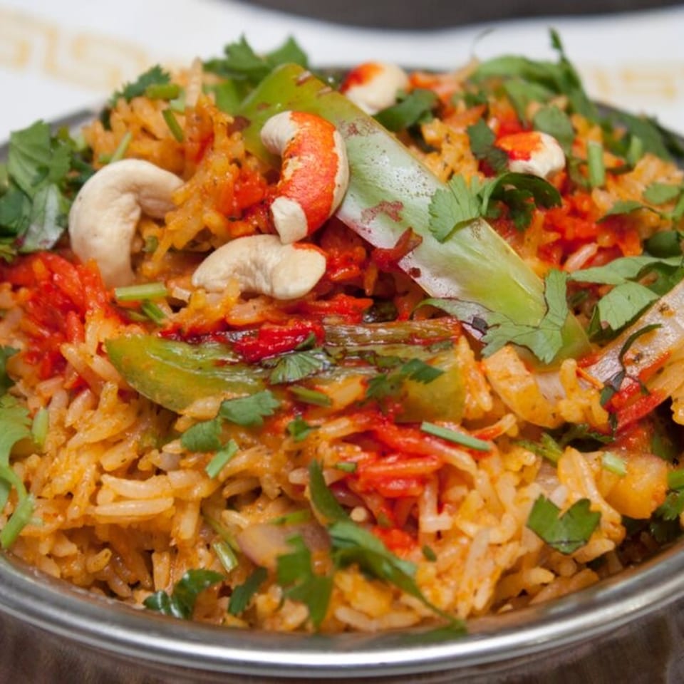 Close-up of Indian biryani with rice, vegetables, cashews, and fresh cilantro in a metal bowl.